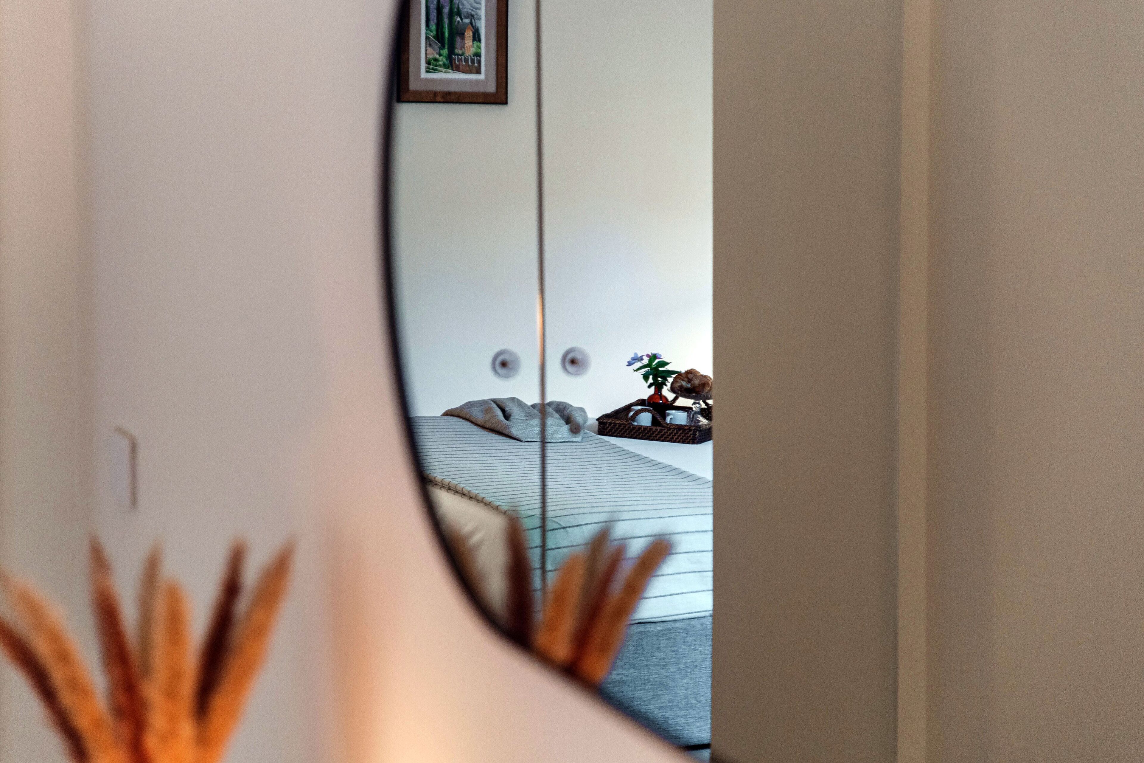 Een slaapkamer met een bed, kussens, een klein tafeltje en een ingelijst schilderij aan de muur.