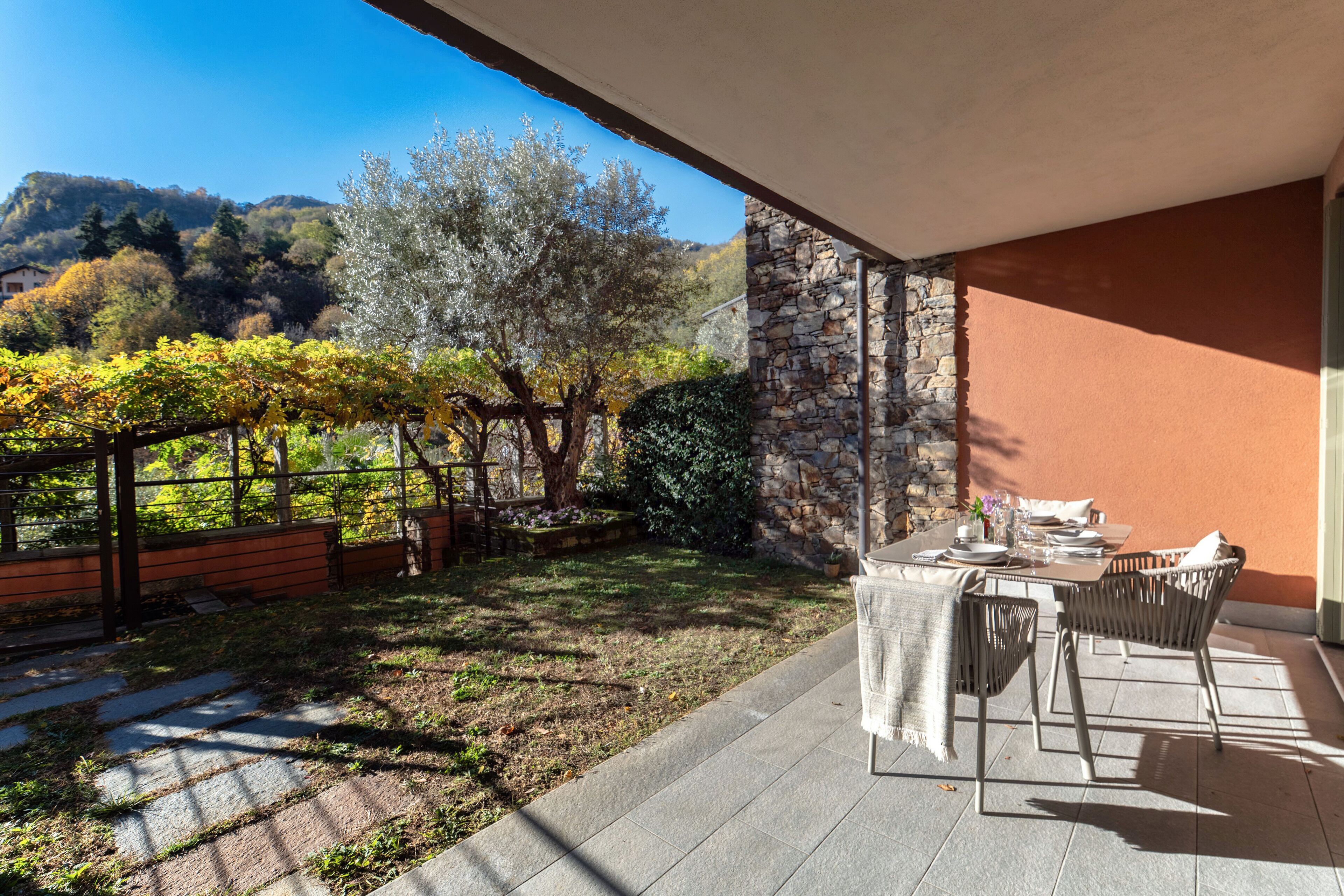 A patio with a table and chairs, a stone wall, and a view of a vineyard and hills.