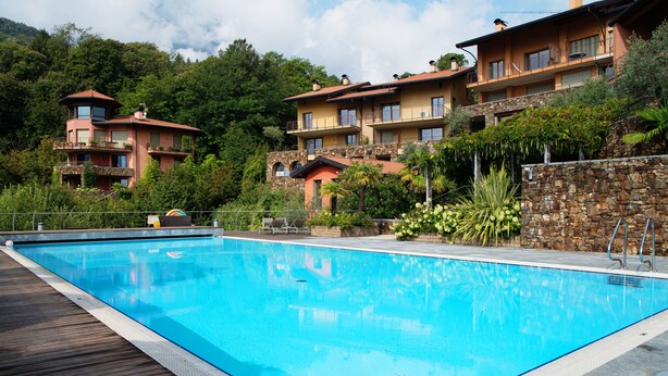 Ein Pool mit Holzterrasse, umgeben von üppiger Vegetation und einer Steinmauer.
