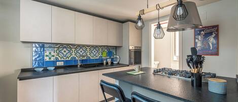 A modern kitchen with a central island, bar stools, a tiled backsplash, and hanging pendant lights.