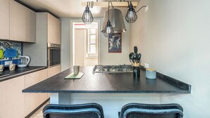 A modern kitchen with a central island, black pendant lights, and a stainless steel stove. - Central City Apartment by Wonderful Italy (Palermo)
