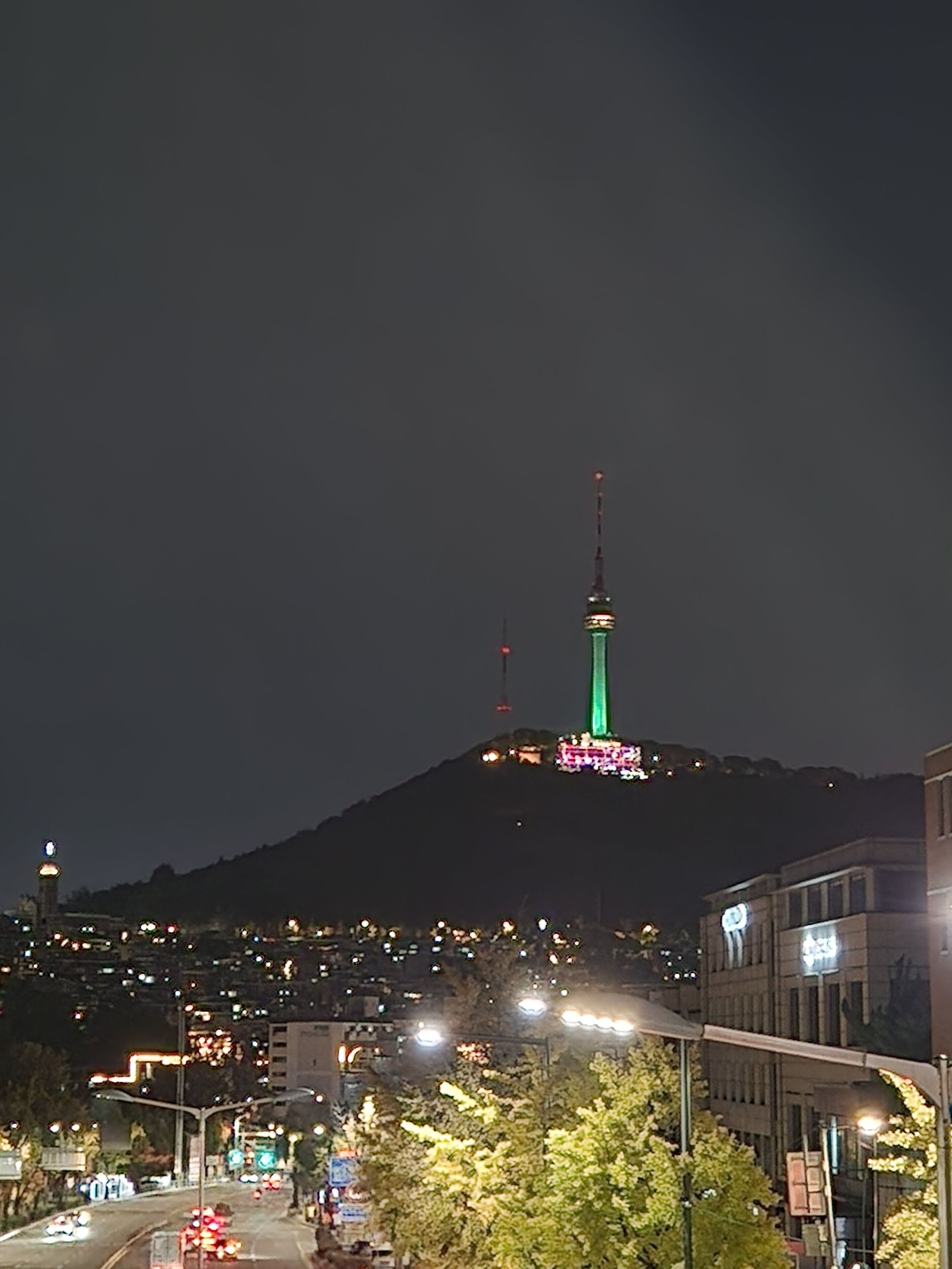 A nighttime cityscape with a prominent tower illuminated in green.