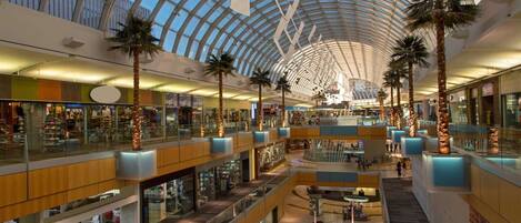 A multi-level shopping mall with a glass ceiling, palm trees, and various retail stores.