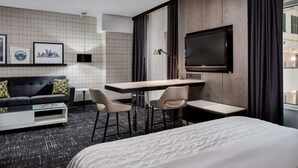A hotel room with a bed, a desk, two chairs, a sofa, a TV, and framed pictures on the wall. - Steps from Galleria Dallas + Dining. Pool. Gym. (Dallas)