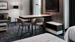 A hotel room with a bed, a desk with two chairs, a TV, and a window with curtains.