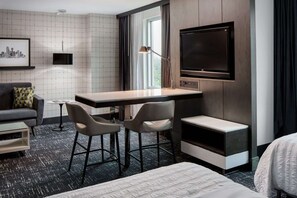 A hotel room with a bed, a desk with two chairs, a TV, and a window with curtains. - Across Galleria Dallas + Dining. Pool. Gym. (Dallas)