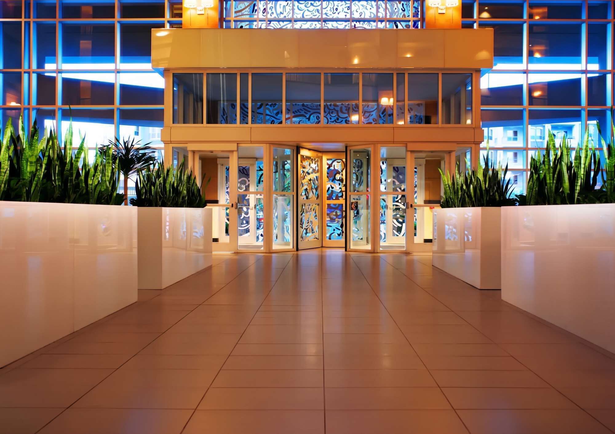 A hotel lobby with a modern design, featuring a glass entrance, tiled flooring, and potted plants.