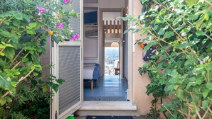 Ein schmaler Eingang zu einem Raum mit einem Bett, einem Sessel und Blick auf einen Balkon.