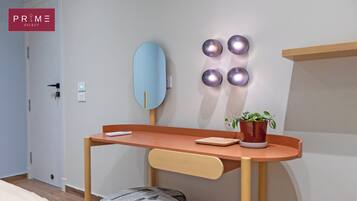 Una habitación moderna con un escritorio de madera, una silla, un pequeño taburete, un espejo adosado a la pared y una planta en maceta.