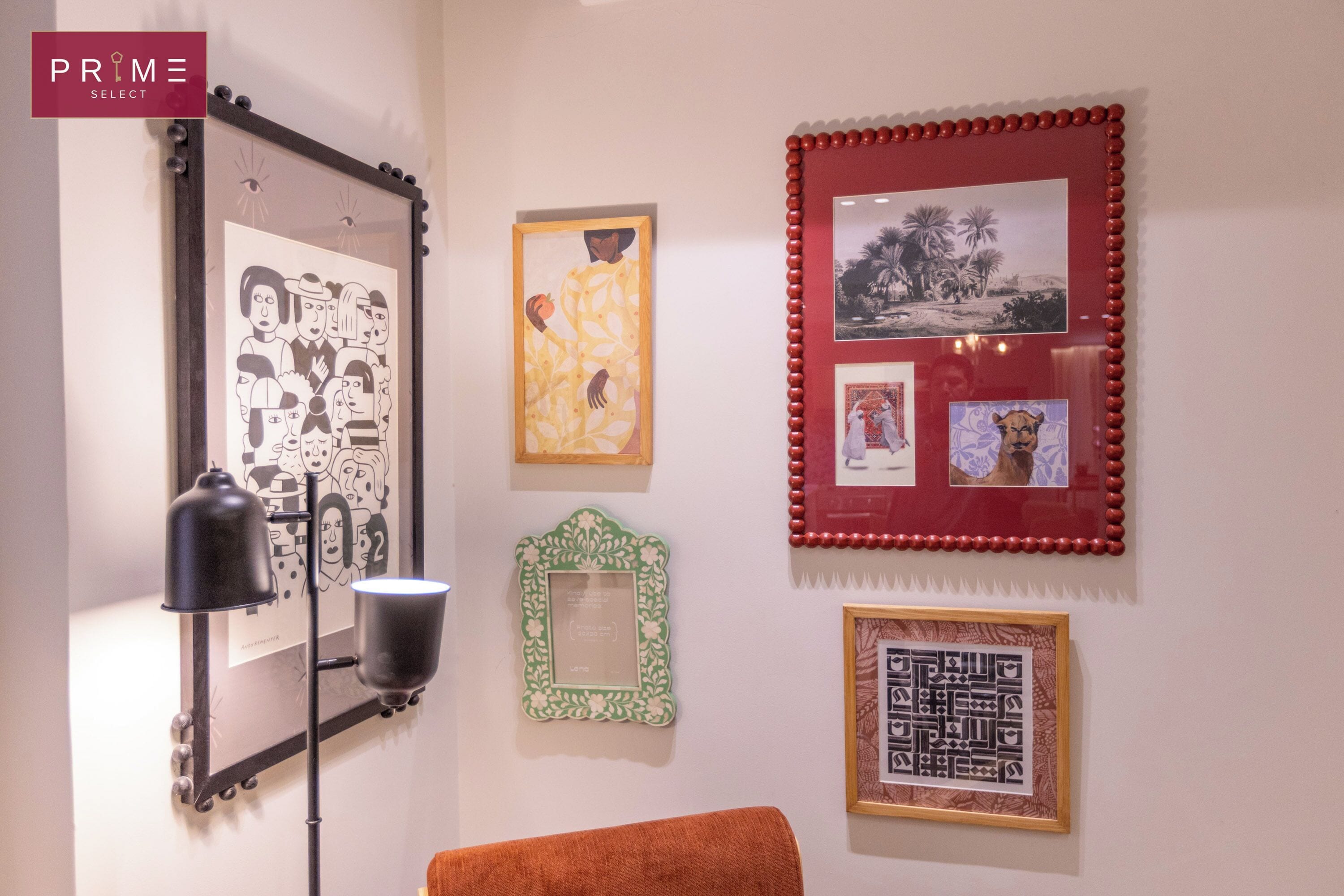 A wall with various framed artworks, including a black and white family portrait, a yellow abstract piece, and a red framed landscape.