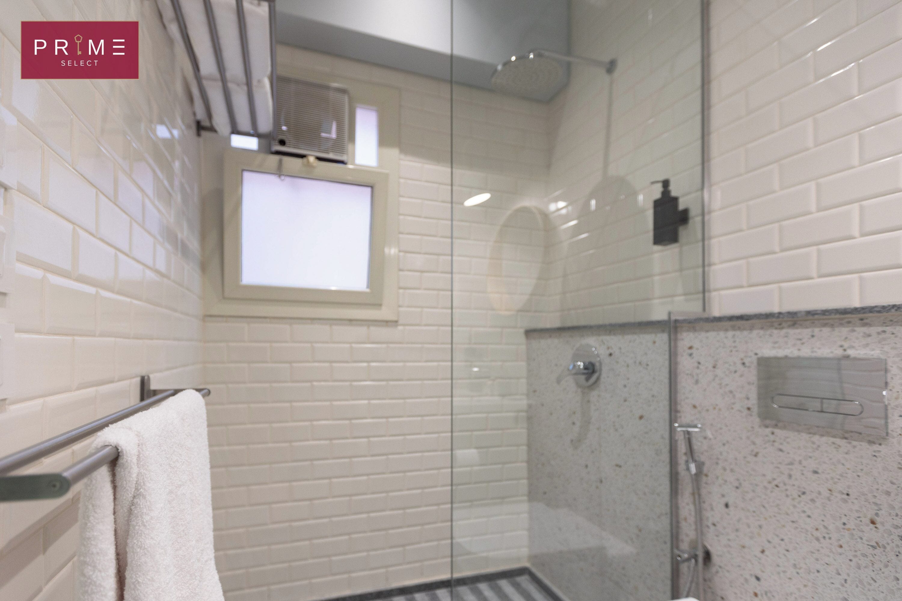 Een moderne badkamer met witte wandtegels, een glazen douchecabine en een zichtbare airconditioner.