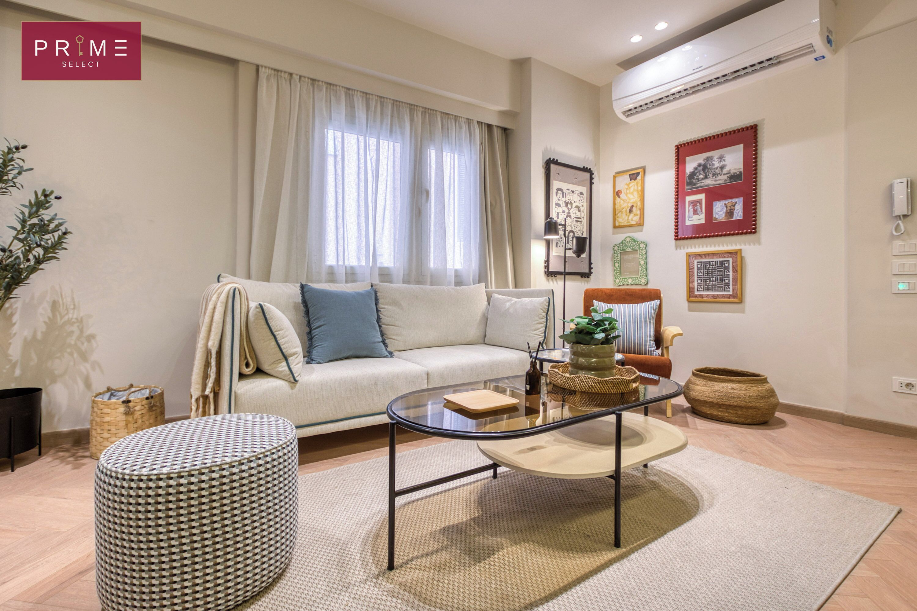 A modern living room with a sofa, a glass coffee table, and a round ottoman.