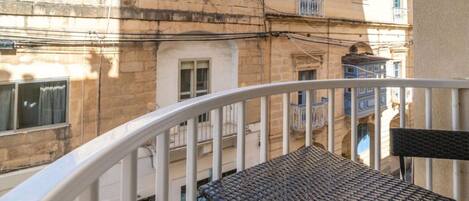 A balcony with two wicker chairs and a white railing, overlooking a building with multiple windows and balconies.