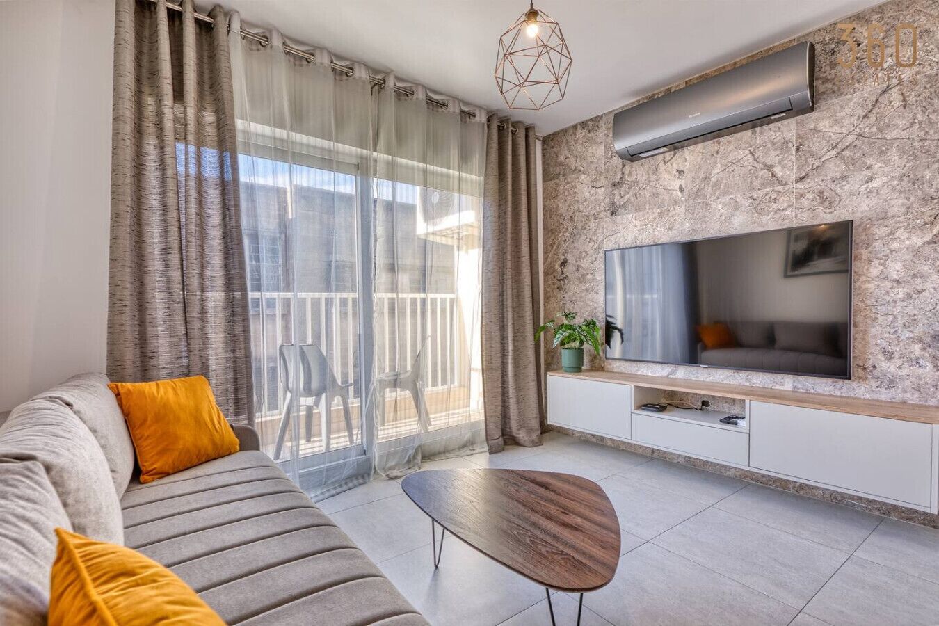 Un salon moderne avec un canapé, une table basse, un téléviseur et un balcon agrémenté de rideaux.