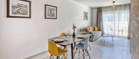 Un comedor con una mesa dispuesta para dos personas, un sofá con cojines y un balcón con cortinas.