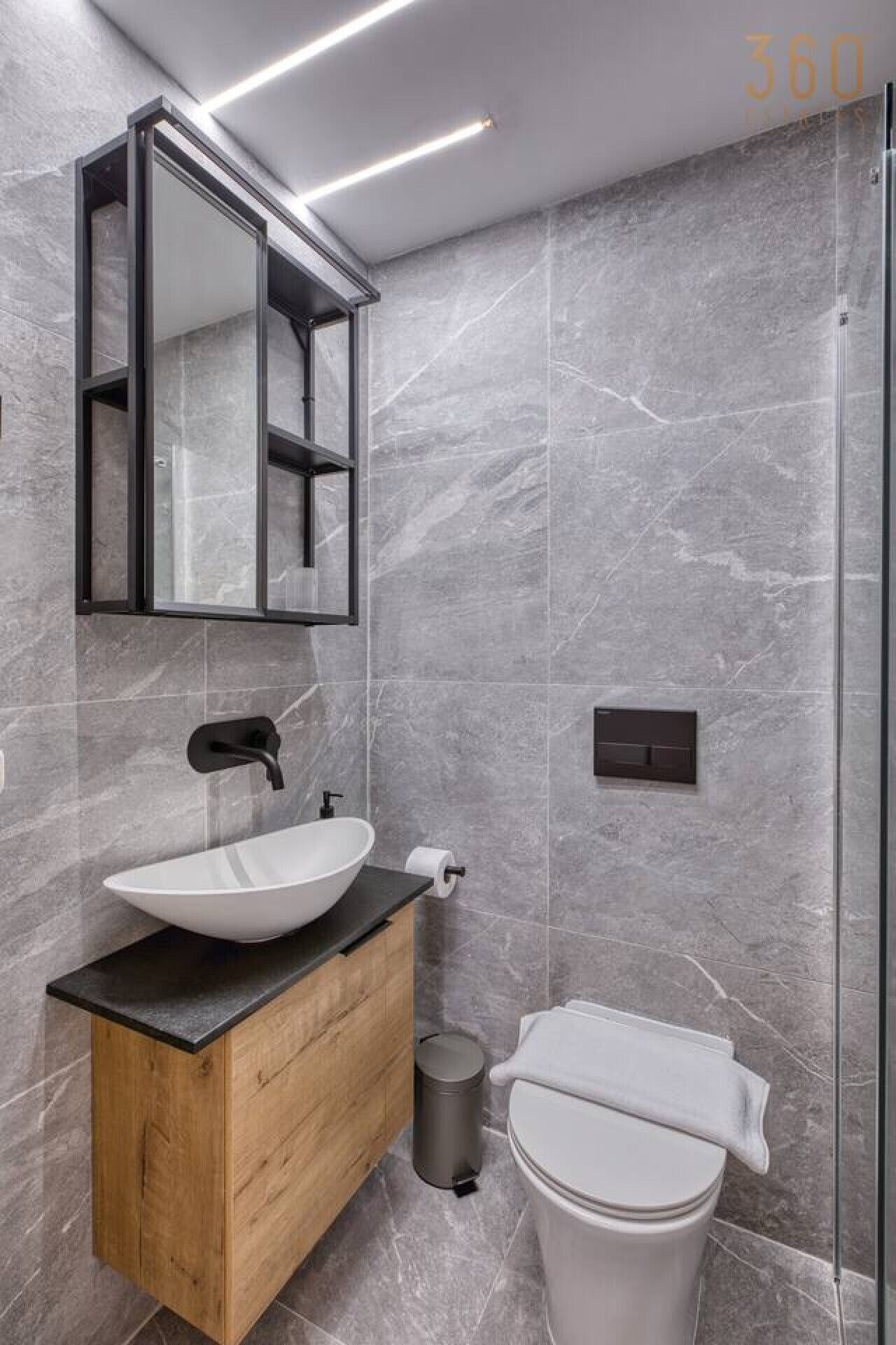 Une salle de bain moderne avec un meuble-lavabo en bois, un lavabo blanc, un robinet noir, un miroir et des toilettes.