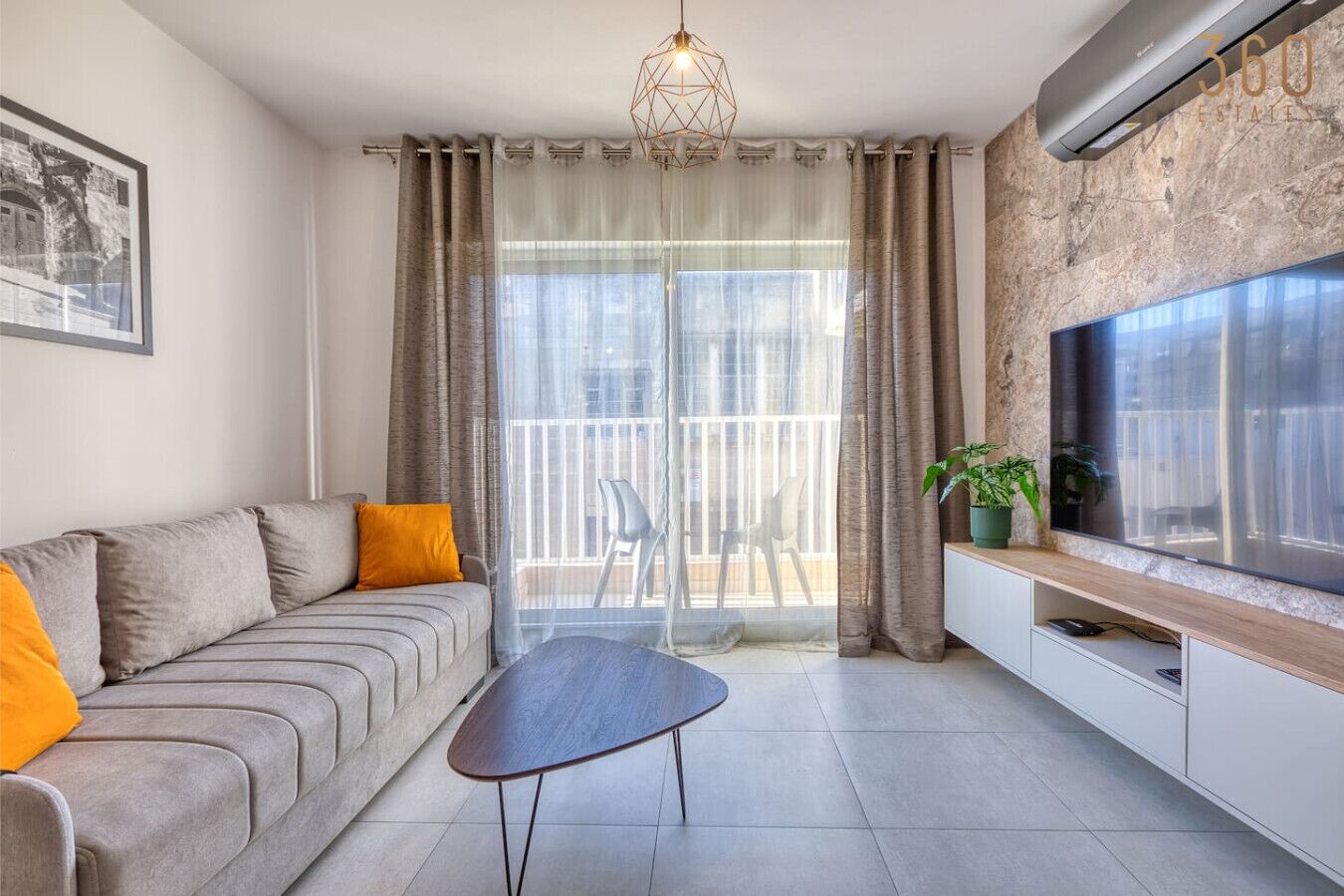 A modern living room with a grey sofa, a wooden coffee table, a TV on a wooden cabinet, and a balcony with a view.