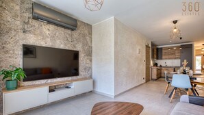 A modern living room with a flat-screen TV, a wooden coffee table, and a dining area with chairs and a table. - Central 2BR Home in Pieta`s Heart w/Wifi & AC ! (Pietà)