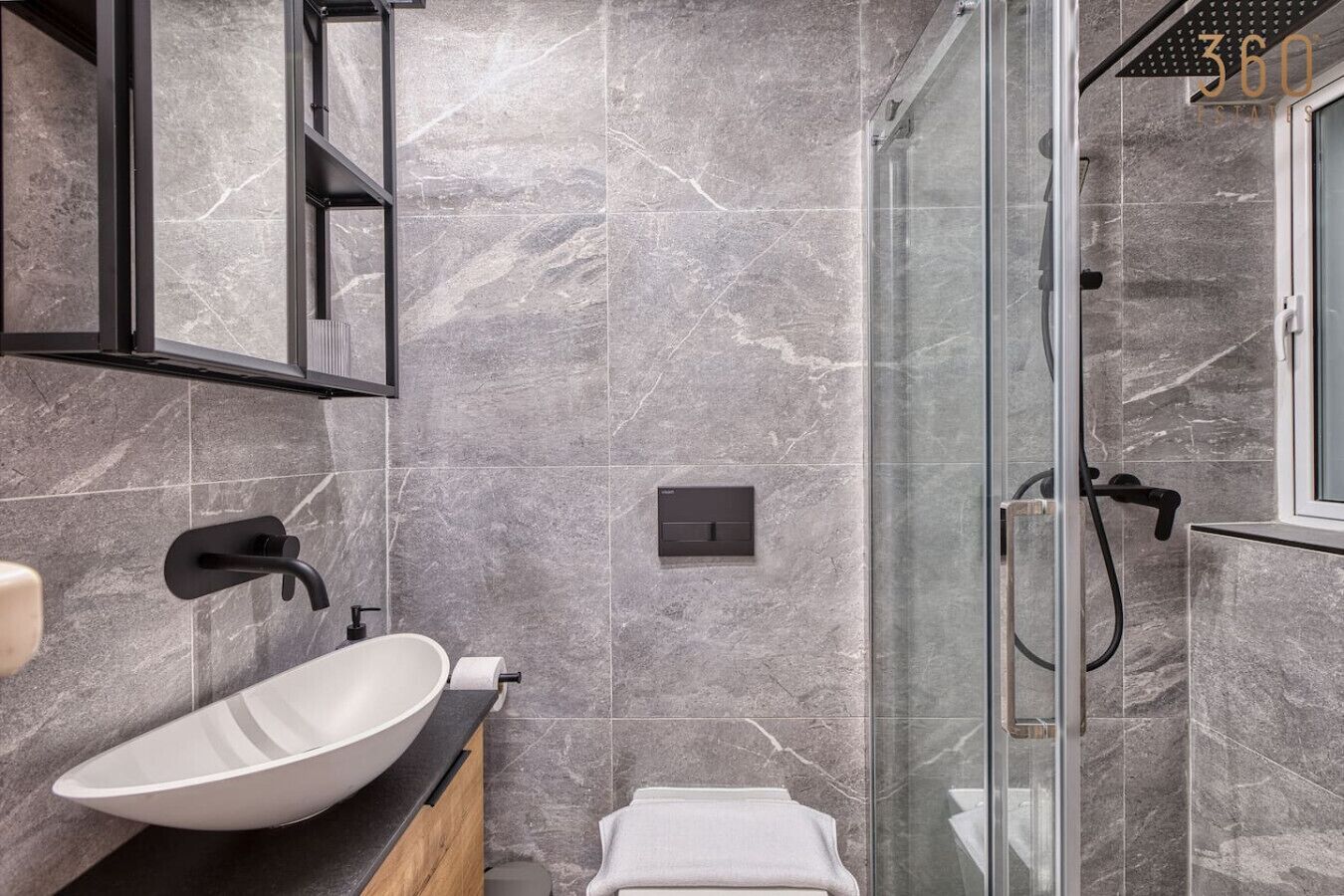 Une salle de bain moderne avec un grand lavabo blanc, une douche en verre et un mur recouvert de carreaux de marbre.