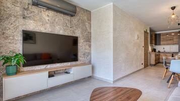 A modern living room with a flat-screen TV, a wooden coffee table, and a dining area with chairs and a table.