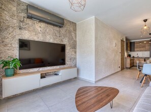 A modern living room with a flat-screen TV, a wooden coffee table, and a dining area with chairs and a table. - Central 2BR Home in Pieta`s Heart w/Wifi & AC ! (Pietà)