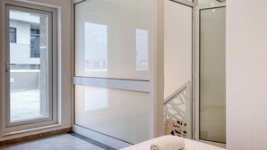 A modern bathroom with a glass shower enclosure, a visible cityscape through the window, and a white towel on the floor.