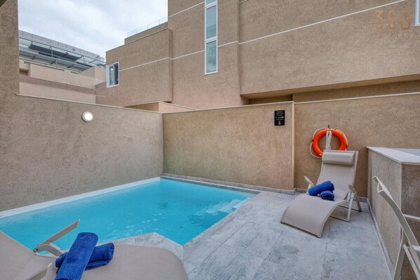 A rooftop pool area with a clear blue pool, lounge chairs, and a lifebuoy.