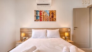 A hotel room with a large bed, two bedside lamps, a painting on the wall, and a door on the right.