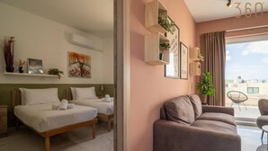 A modern hotel room with two beds, a sofa, a dining area, and a balcony with a view. - Peaceful 2BR Penthouse with Terrace Views & Beach (Marsaskala)