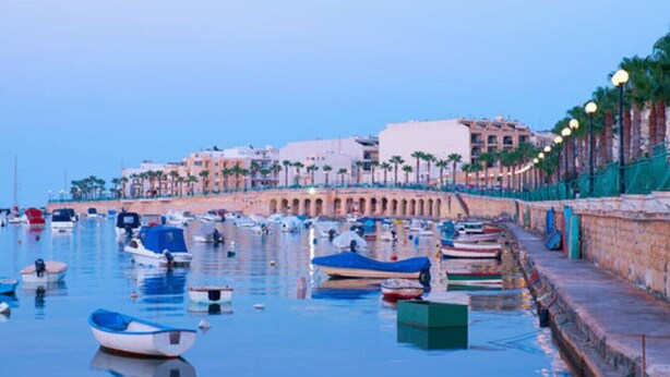 A marina with boats docked along a waterfront promenade, featuring a stone wall and palm trees. - Peaceful 2BR Penthouse with Terrace Views & Beach (Marsaskala)