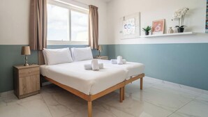 A bedroom with a bed, nightstands, a wardrobe, a window with curtains, and wall-mounted shelves with plants and artwork. - Peaceful 2BR Penthouse with Terrace Views & Beach (Marsaskala)