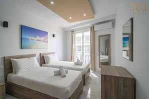 Habitación de hotel con dos camas, un ventanal grande y un cuadro de una escena costera.