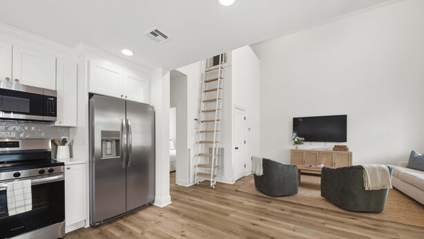Una cocina moderna con electrodomésticos de acero inoxidable, piso de madera e interiores blancos.