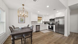 Una cocina moderna con armarios blancos, electrodomésticos de acero inoxidable y una mesa de comedor de madera.