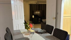 Een eetgedeelte met een tafel gedekt voor vier personen, een televisie op de achtergrond en een deur naar een andere kamer.