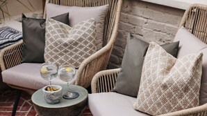 A wicker chair with grey cushions, a small round table with a bowl and glasses, and a brick floor. - Beautiful Fulham Townhouse with a bar & pool table (Parsons Green, London, UK)