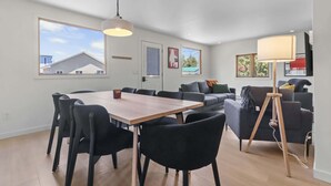 A modern living room with a dining area, large windows, and a floor lamp. - Beach & Comfort | La Trappe a Houmard (Pointe-du-Chêne)