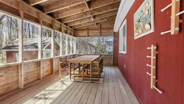 A covered wooden deck with a dining table and chairs, large windows, and a red wall with a decorative plate rack. - Beach & Comfort | La Trappe a Houmard (Pointe-du-Chêne)