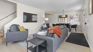 A modern living room with a grey sofa, a coffee table, and a staircase. - Beach & Comfort | La Trappe a Houmard (Pointe-du-Chêne)