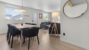 A modern living room with a dining table, chairs, a sofa, and a lamp. - Beach & Comfort | La Trappe a Houmard (Pointe-du-Chêne)