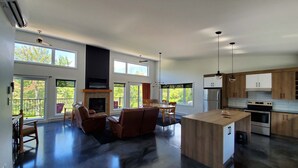 Amplia sala de estar con chimenea, ventanas grandes y una cocina moderna con electrodomésticos de acero inoxidable.