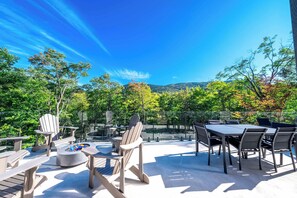 Eine Terrasse im Freien mit Adirondack-Stühlen, einer runden Feuerstelle und einem Esstisch mit Stühlen.