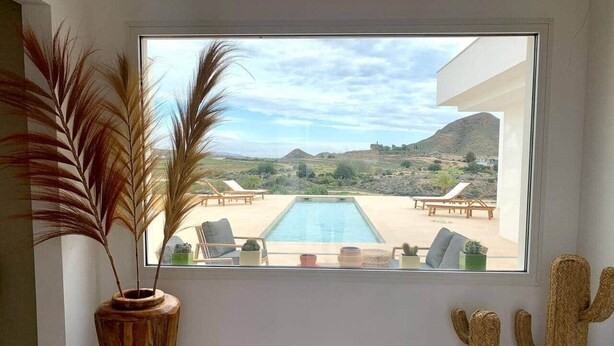 Habitación con un amplio ventanal con vistas a una piscina y zona de estar al aire libre.