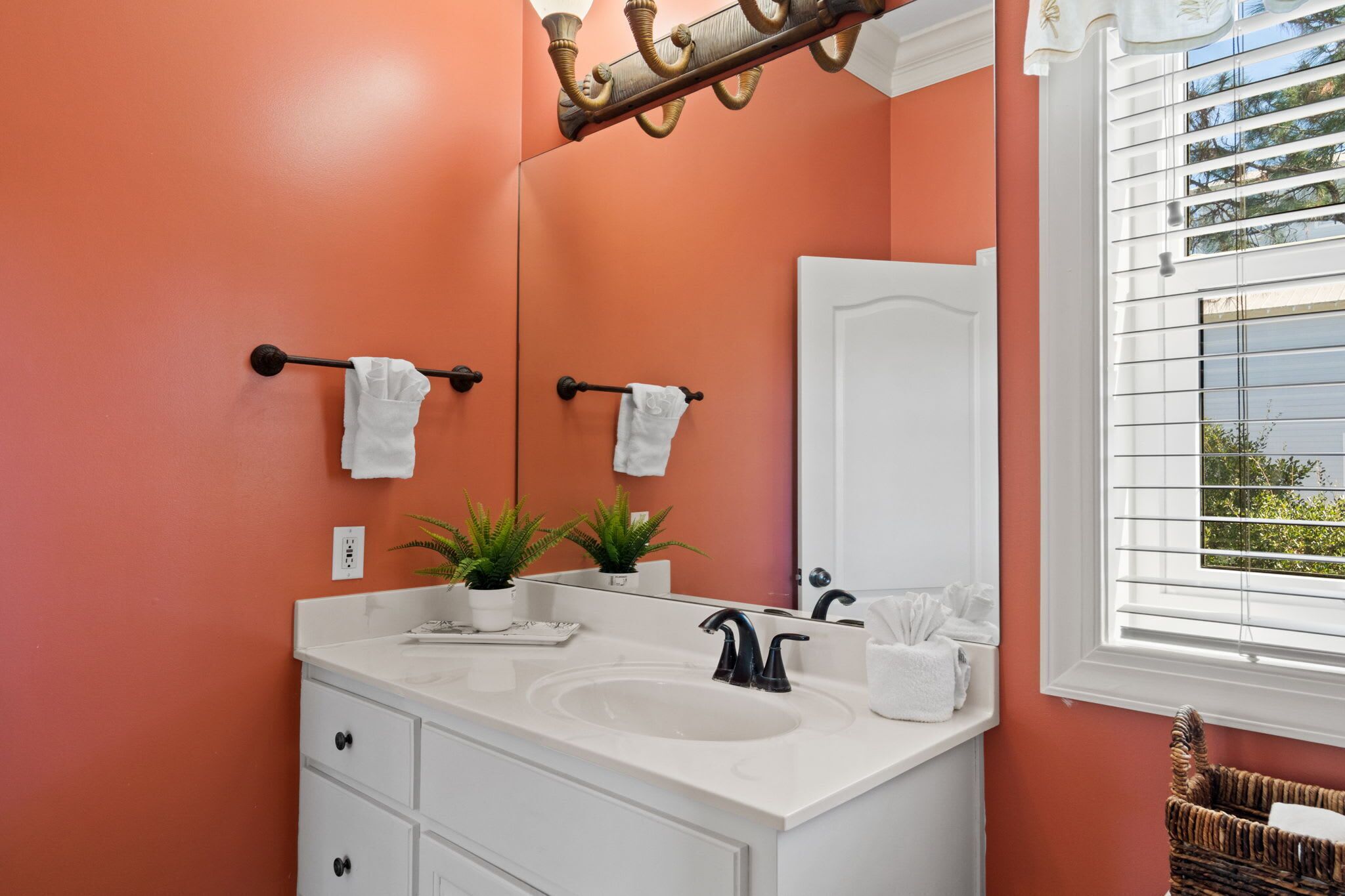 A bathroom with a white vanity, a large mirror, and a window with blinds.