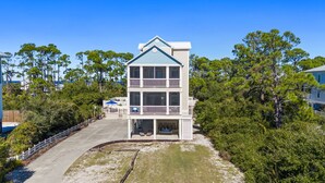 A two-story building with a balcony on the upper floor, surrounded by trees and a sandy area. - Salty Daze- Private pool & hot tub, pet friendly, family friendly! (Cape San Blas)