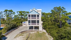 A two-story building with a balcony on the upper floor, surrounded by trees and a sandy area. - Salty Daze- Private pool & hot tub, pet friendly, family friendly! (Cape San Blas)