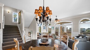 A spacious living area with a dark wooden dining table, white chairs, a chandelier, and a staircase leading to another level. - Salty Daze- Private pool & hot tub, pet friendly, family friendly! (Cape San Blas)