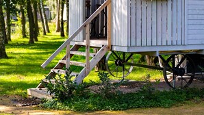 Een houten vakantiehuisje met een veranda en trap, omringd door bomen.