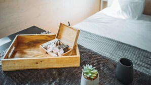 Een net opgemaakt bed met een houten nachtkastje waarop een verzorgingsset en een kleine potplant staan.