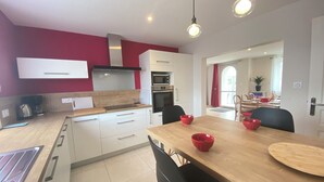 A modern kitchen with white cabinets, a wooden countertop, and a dining area with a wooden table and black chairs. - Spacious house, all comforts, beach and harbour 100 metres away (Plouescat)